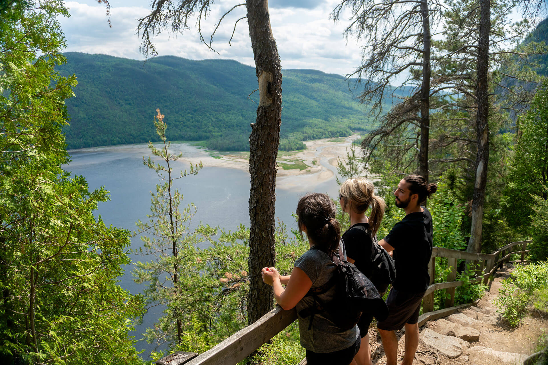Trois personnes, deux femmes et un homme admirant le Fjord du Saguenay d'un point de vue du parc national.