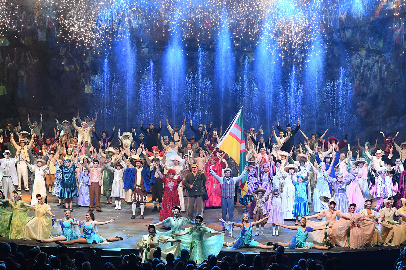 Une centaine de comédiens en costume d'époque sur la scène de la Fabuleuse Histoire d'un Royaume dont un portant fièrement le drapeau du Saguenay-Lac-Saint-Jean.